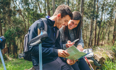 Young couple doing trekking sitting looking mobile and map outdoors
