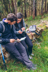 Young couple doing trekking sitting looking mobile and map outdoors