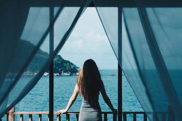 Woman open the curtain in the room looking to outside sea view.