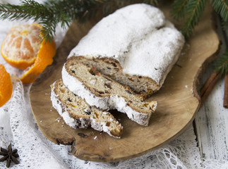 Traditional European Christmas pastry, fragrant home baked stollen, with spices and dried fruit. Sliced on wooden table with xmas tree branches and decorations, copy space