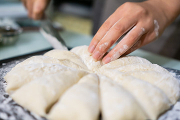 Obraz na płótnie Canvas Cutting raw dough in flour with a knife (close-up of hands cutting dough)