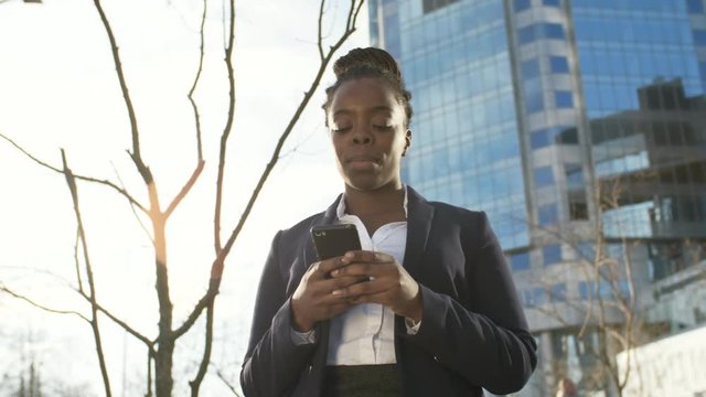 Low angle view of African businesswoman standing outdoors and using smartphone
