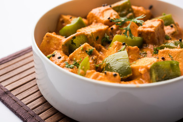 Malai or achari Paneer in a gravy made using red gravy and green capsicum. served in a bowl. selective focus