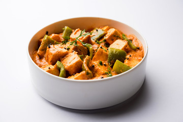 Malai or achari Paneer in a gravy made using red gravy and green capsicum. served in a bowl. selective focus