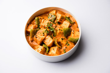 Malai or achari Paneer in a gravy made using red gravy and green capsicum. served in a bowl. selective focus