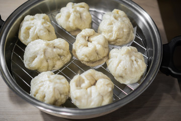 Chinese dumplings (buns) being steamed on a modern stainless steel wok pan