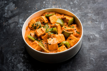 Malai or achari Paneer in a gravy made using red gravy and green capsicum. served in a bowl. selective focus