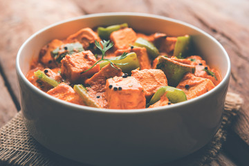 Malai or achari Paneer in a gravy made using red gravy and green capsicum. served in a bowl. selective focus