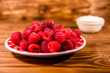 Ceramic plate with ripe raspberries and sour cream on wooden table