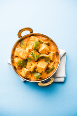 Malai or achari Paneer in a gravy made using red gravy and green capsicum. served in a bowl. selective focus