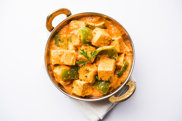 Malai or achari Paneer in a gravy made using red gravy and green capsicum. served in a bowl. selective focus