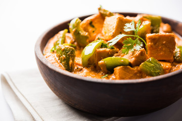Malai or achari Paneer in a gravy made using red gravy and green capsicum. served in a bowl. selective focus