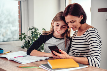 Mother using smart phone and helping daughter with homework