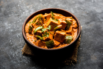 Malai or achari Paneer in a gravy made using red gravy and green capsicum. served in a bowl. selective focus