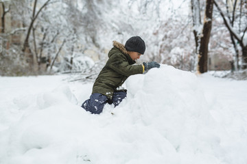 Fototapeta na wymiar cute little boy making snowman in snow outdoor