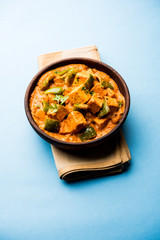 Malai or achari Paneer in a gravy made using red gravy and green capsicum. served in a bowl. selective focus