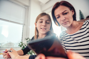 Mother using smart phone and helping daughter with homework