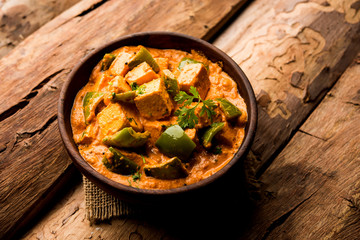Malai or achari Paneer in a gravy made using red gravy and green capsicum. served in a bowl. selective focus