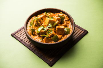 Malai or achari Paneer in a gravy made using red gravy and green capsicum. served in a bowl. selective focus