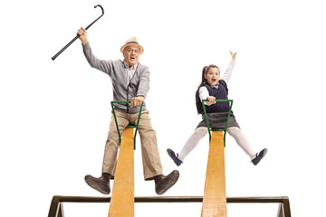 Cheerful grandpa and his granddaughter having fun on a seesaw