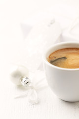 A cup of coffee and a small Christmas bauble and white wooden background. Close up. Copy space. 
