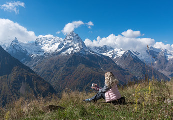 Naklejka na ściany i meble woman traveler drinks coffee with a view of the mountain landscape. A young tourist woman drinks a hot drink from a cup and enjoys the scenery in the mountains. Trekking concept.