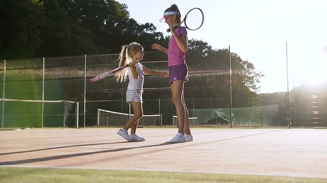 Little tennis player giving five to cute female coach and hugging after tennis training on the court. - Powered by Adobe