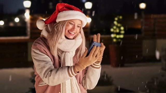 Beautiful blonde woman in warm clothes using smartphone to make selfie in snow street