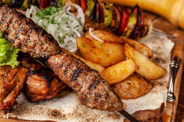 The concept of Georgian cuisine. Meat board with shashlik, grilled pork ribs, lulya kebab and shish kebab. Grilled french fries and grilled vegetables. Meat feed on a wooden board.