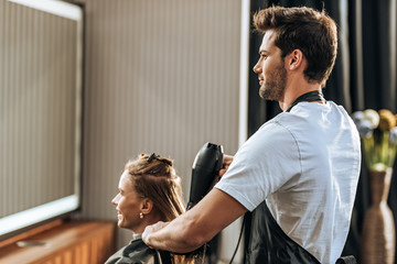 Handsome young hairdresser drying hair to girl in beauty salon
