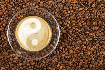 Cup of espresso with yin-yang sign on coffee foam on coffee beans background. With copy space