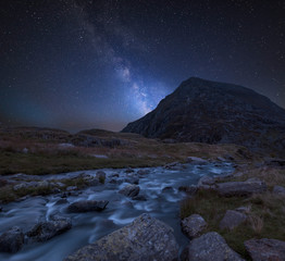 Digital composite Milky Way image of Moody landscape image of river flowing down mountain range near Llyn Ogwen and Llyn Idwal in Snowdonia