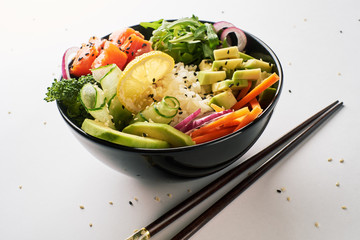 poke bowl with salmon, avocado, cucumber, arugula, broccoli, rice, carrot and sweet onions with chopsticks isolated over white background. side view