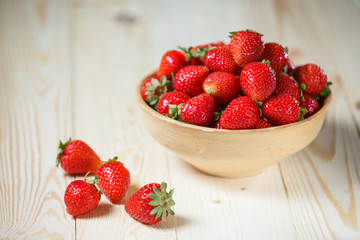 Fresh strawberries in a bowl on wooden table with low key scene.