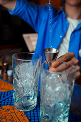Barmen hand with shaker  pouring cocktail into glass, on bright background