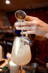 Barmen hand with shaker  pouring cocktail into glass, on bright background