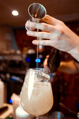 Barmen hand with shaker  pouring cocktail into glass, on bright background