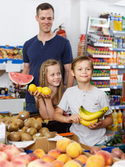 Smiling family with kids looking for fresh delicious fruits in shop
