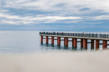 Fototapeta na wymiar Sea pier. Fishermen fishing on the pier. Sea and clouds above