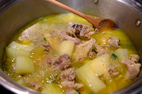 A Filipino food dish called "Tinolang Manok". Close up of Filipino home made Tinolang Manok soup with chicken, papaya, noodles, broth, and green onions. A wooden spoon is present.
