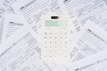 top view of white calculator with tax forms on background