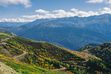 Fototapeta na wymiar The slopes of the mountains are covered with autumn forest shrubs and herbs. Colorful autumn landscape. Warm autumn Sunny day. Clouds over the mountains