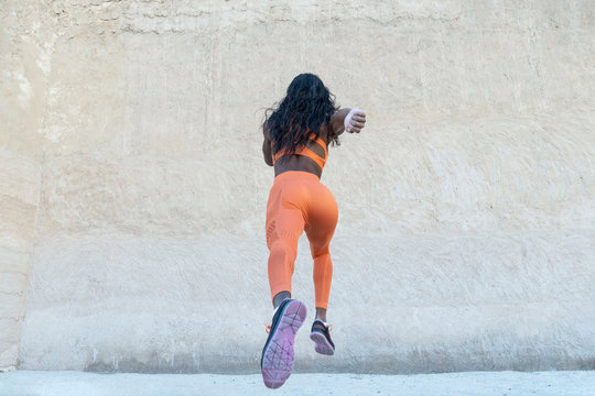 Rare View Of An African American Black Athletic Model Wearing Bright Orange Sports Outfit Does A Dramatic Running Leap Toward A Concrete Wall 