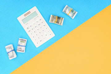 top view of calculator and money rolls on blue and yellow background