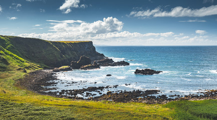 Picturesque Northern Ireland bay. Green grass covered land next to the ocean water. Amazing marine scenery. Blue cloudy sky background. Beauty of the wild untouched nature.