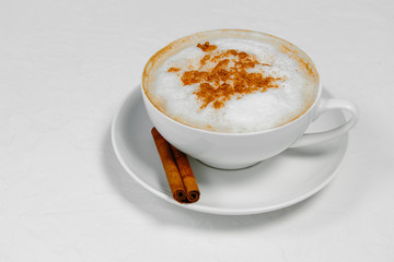 Cup of cappuccino with cinnamon on white background