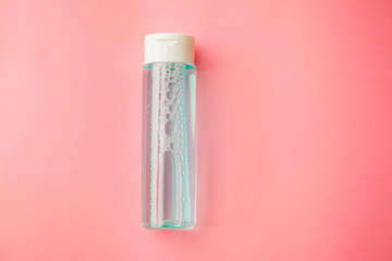 bottle with tonic or micellar cleansing water with fresh herbs and flowers on pink background, top...