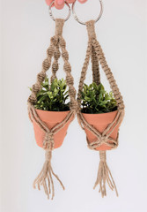 Obraz premium Two mini macrame plant hangers made out of 100% jute twine are being held up by hands. Fake plants are in the ceramic pots.