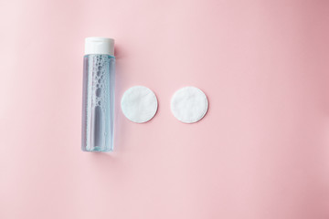 bottle with tonic or micellar cleansing water with fresh herbs and flowers and cotton pads on pink...