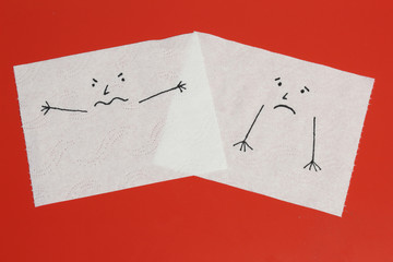 Two white toilet paper pieces sketched with an angry and a melancholic face, close to each others, representing the anger and the sadness feelings